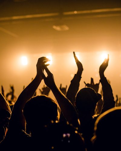 Concert crowd raised hands at rock concert, silhouetted against stage lighting.
